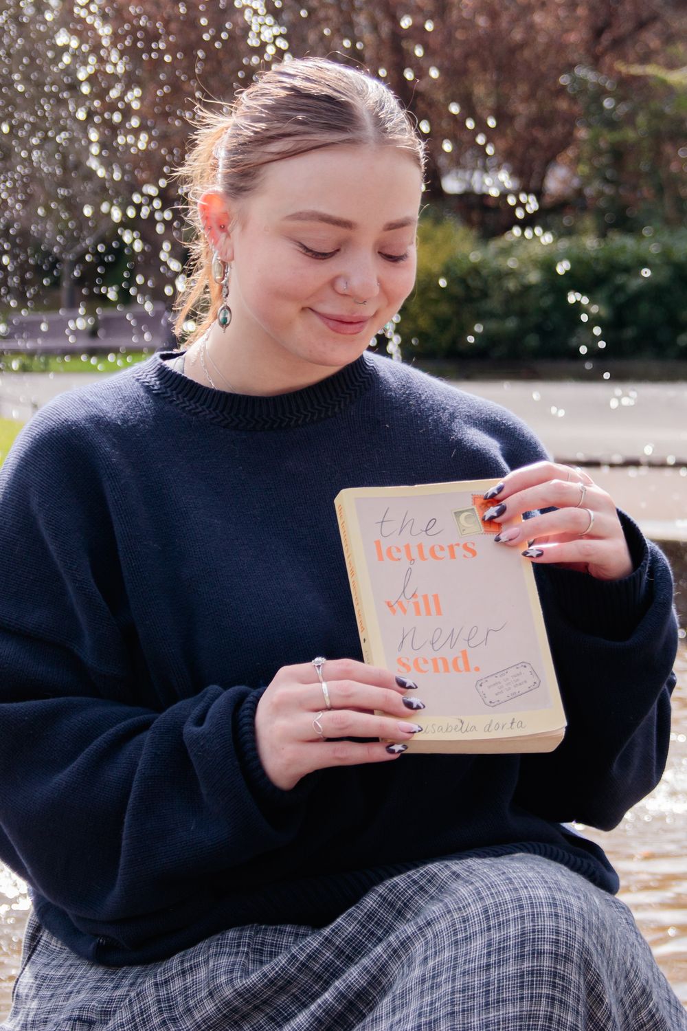 A person in a navy sweater reads a book outdoors with sparkles in the background.