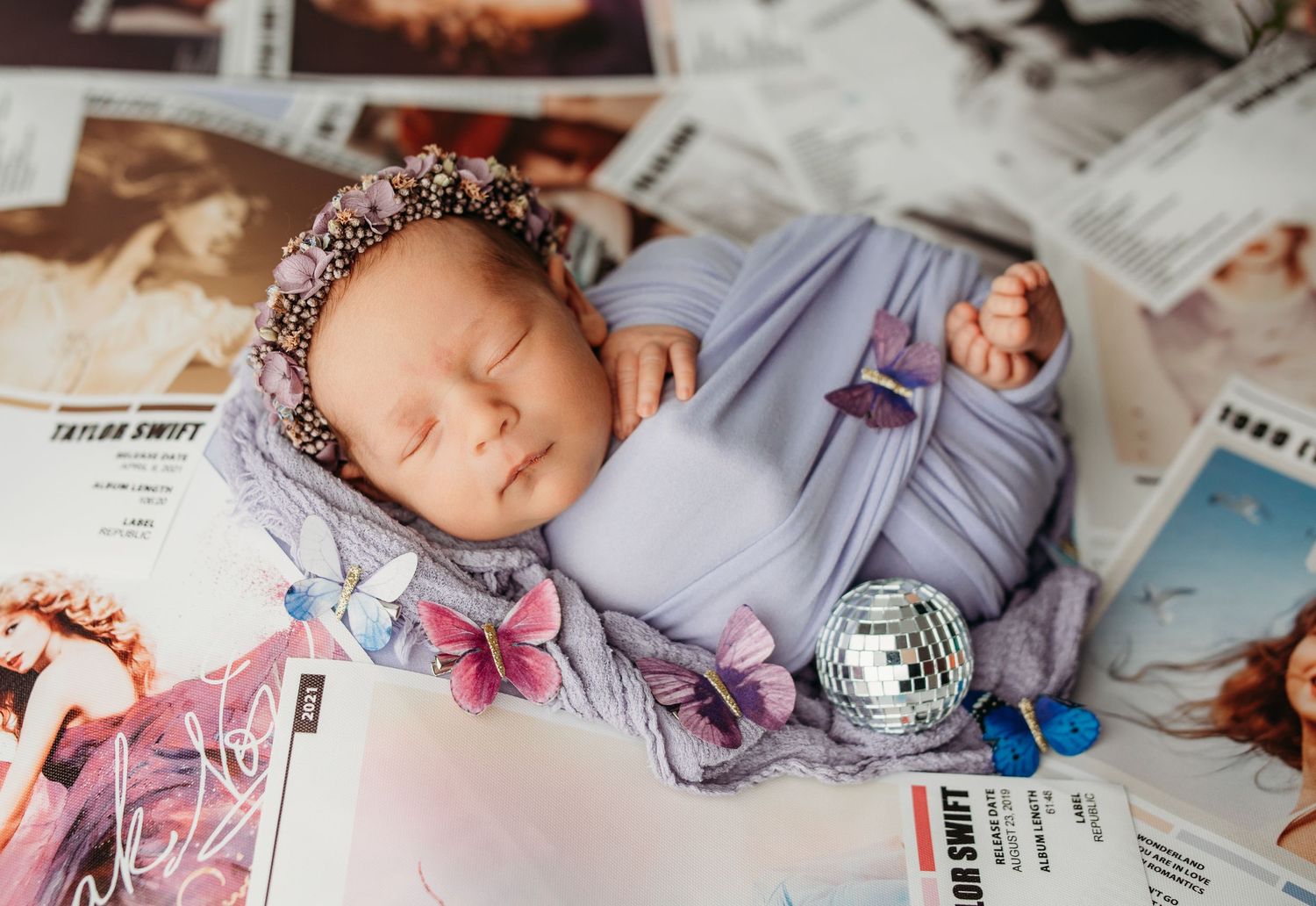 Newborn photography with purple wrap and butterfly decorations against light background.