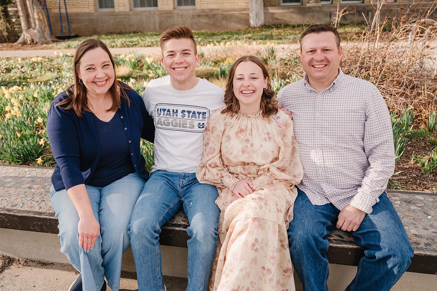 A group of four people sitting together on outdoor steps wearing casual outfits in blue and neutral colors.