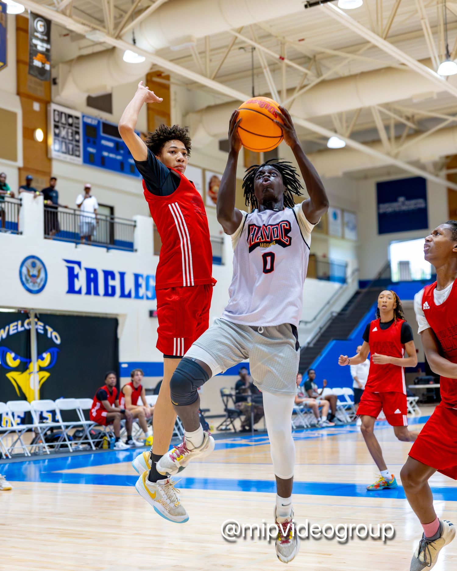 Basketball players compete in an intense game with one player going for a layup against a defender in a red jersey.