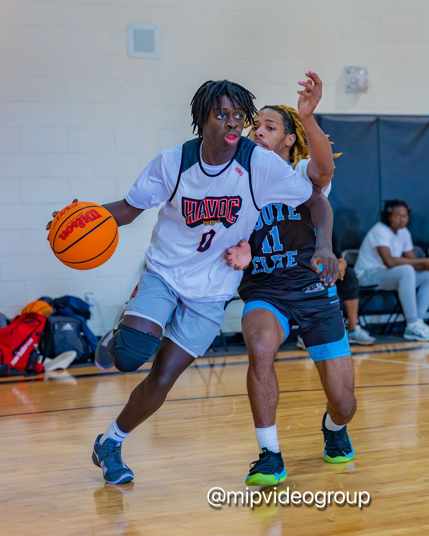 Basketball players compete intensely on an indoor court during a game as spectators watch from the sidelines.