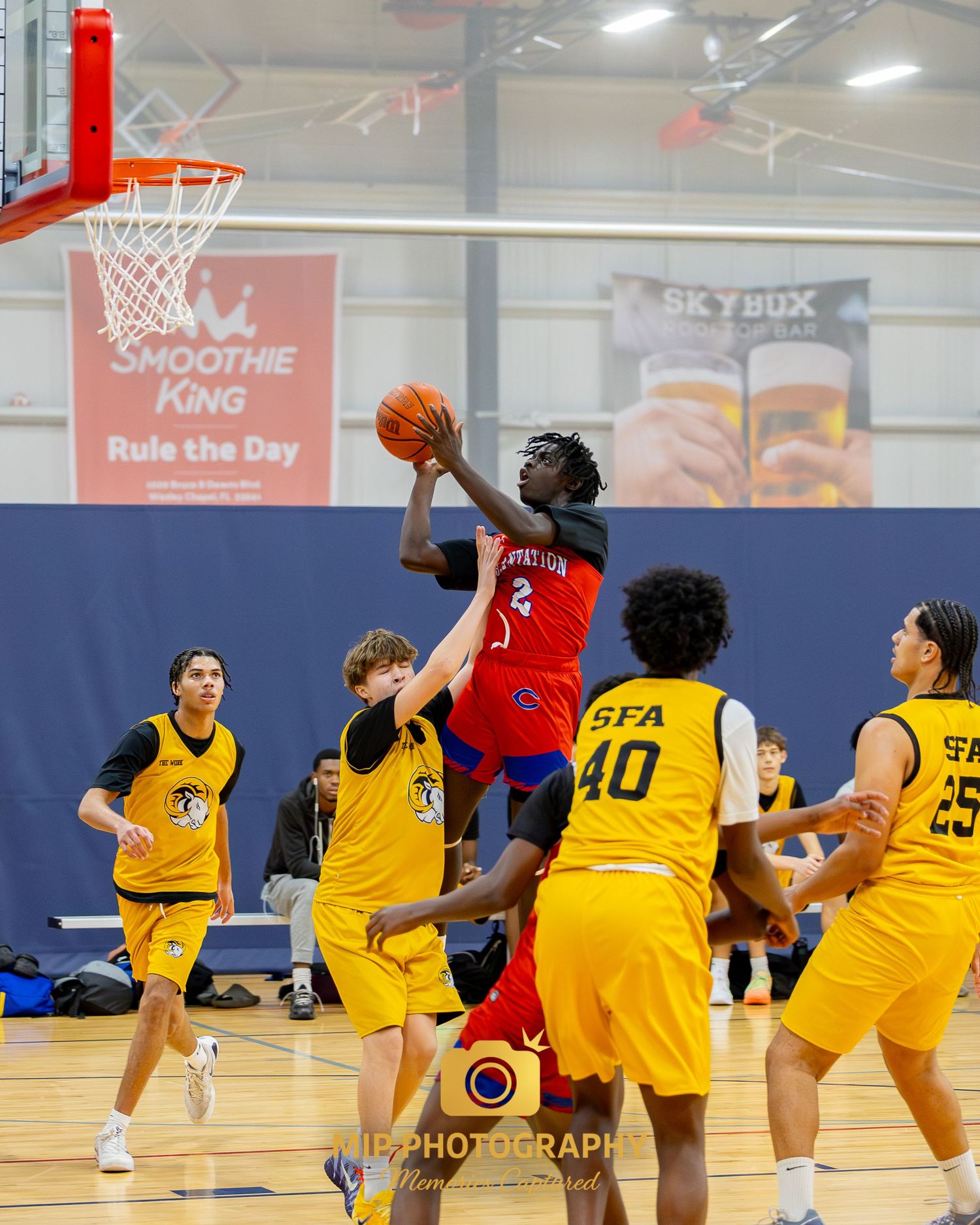 A basketball player in red jumps for a layup while surrounded by defenders in yellow jerseys.
