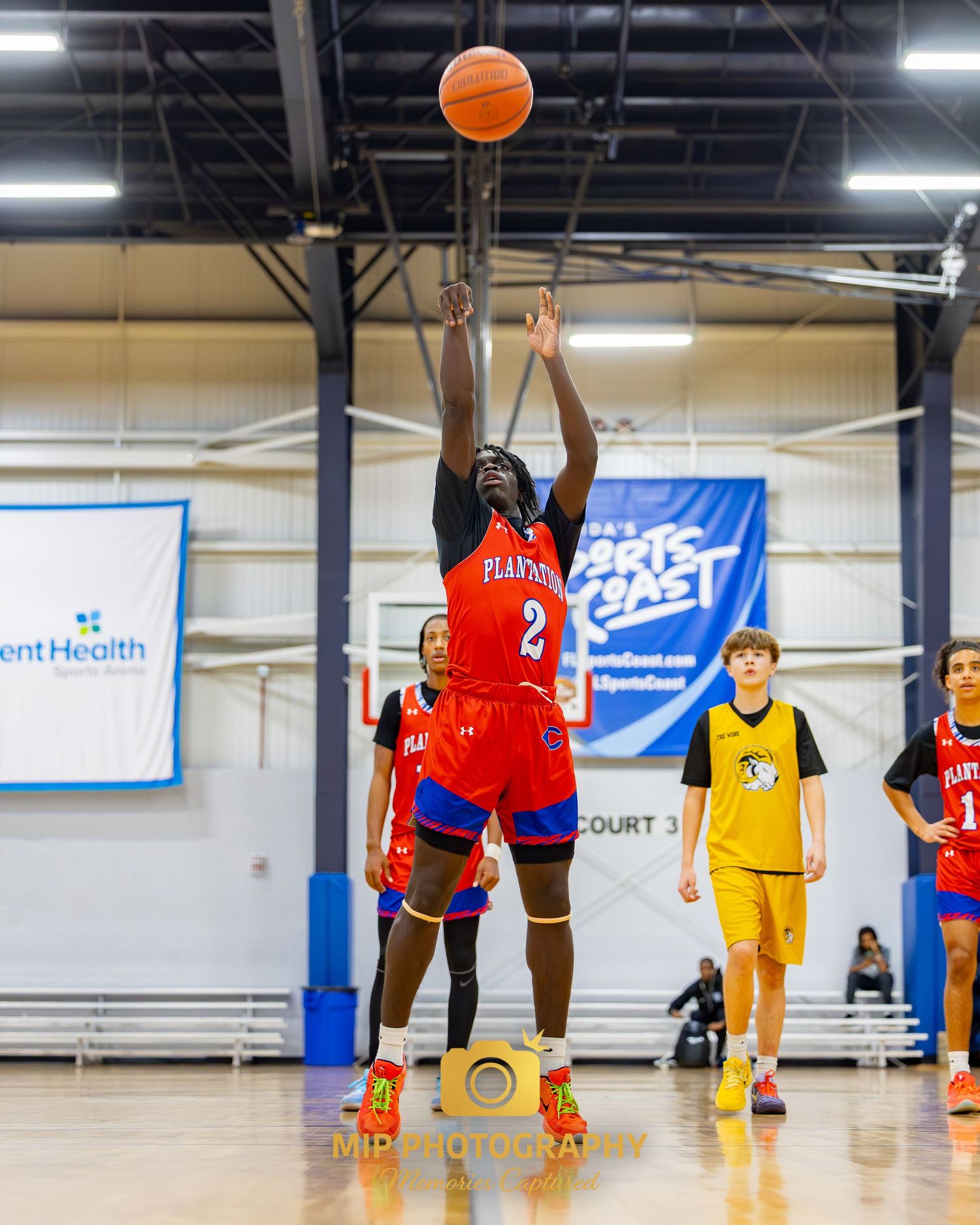 A basketball player in a red jersey shoots the ball during a game in an indoor gymnasium.