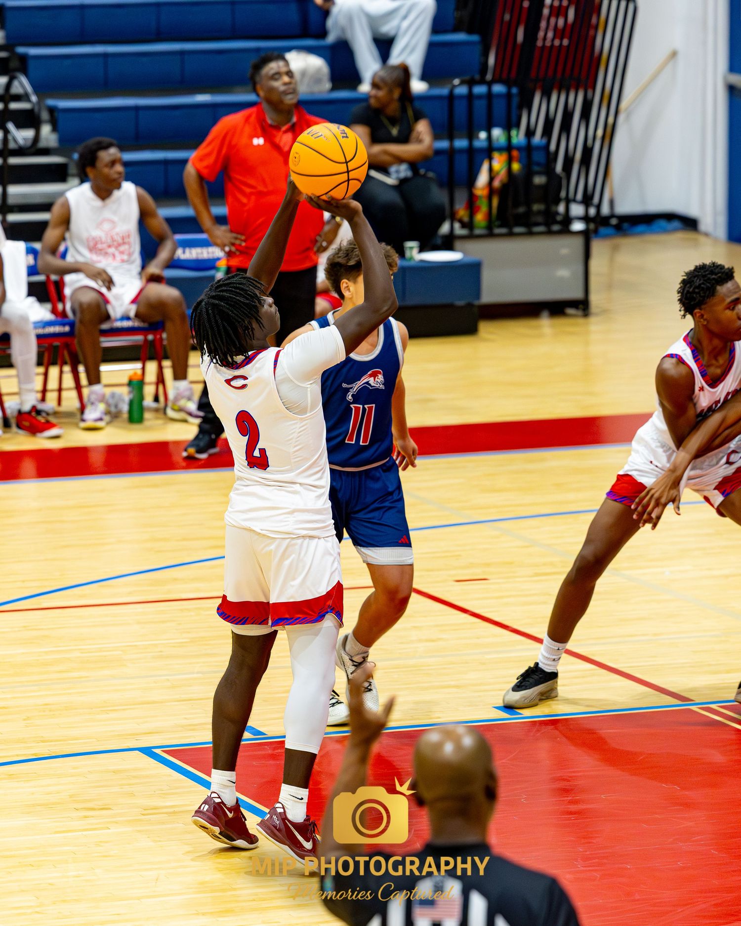 Basketball players compete for possession during an intense indoor game with a referee watching.