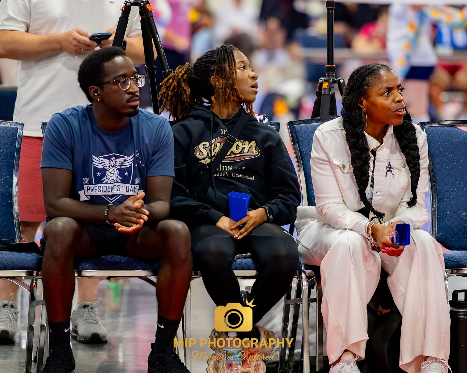 People sitting on sideline chairs watching a sporting event in a gymnasium or indoor arena.