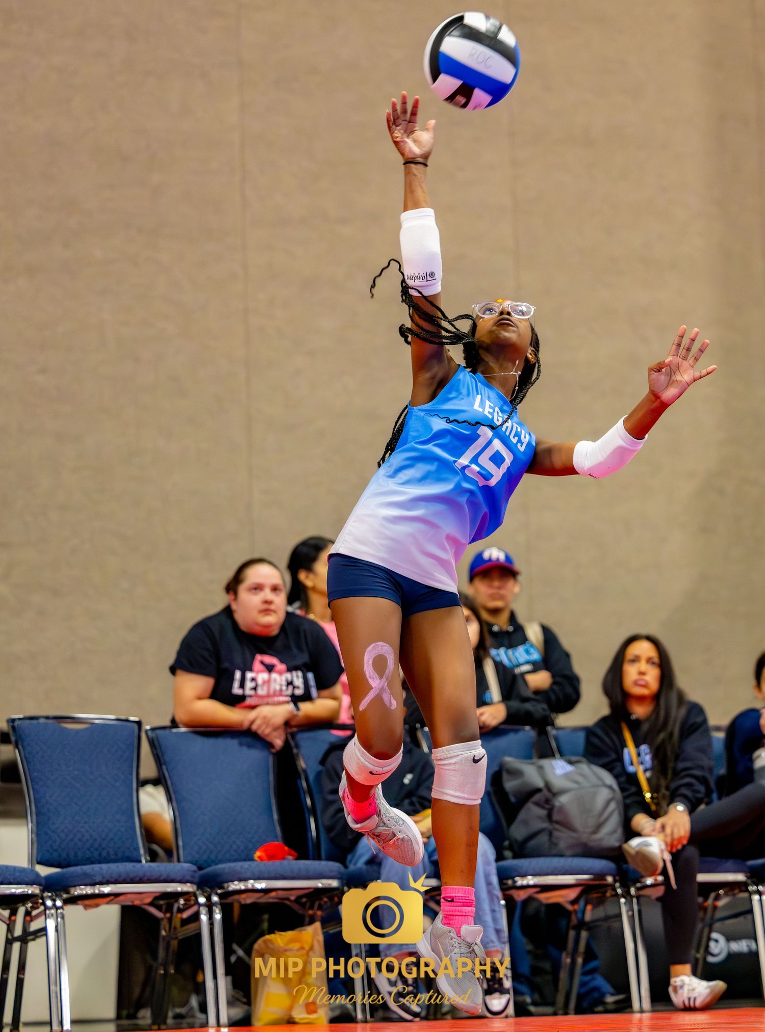 A volleyball player leaps to make a play on the ball during an indoor match with spectators watching.