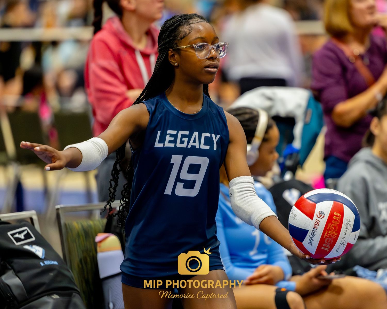Volleyball player wearing navy blue Legacy jersey number 19 prepares to serve during indoor match.