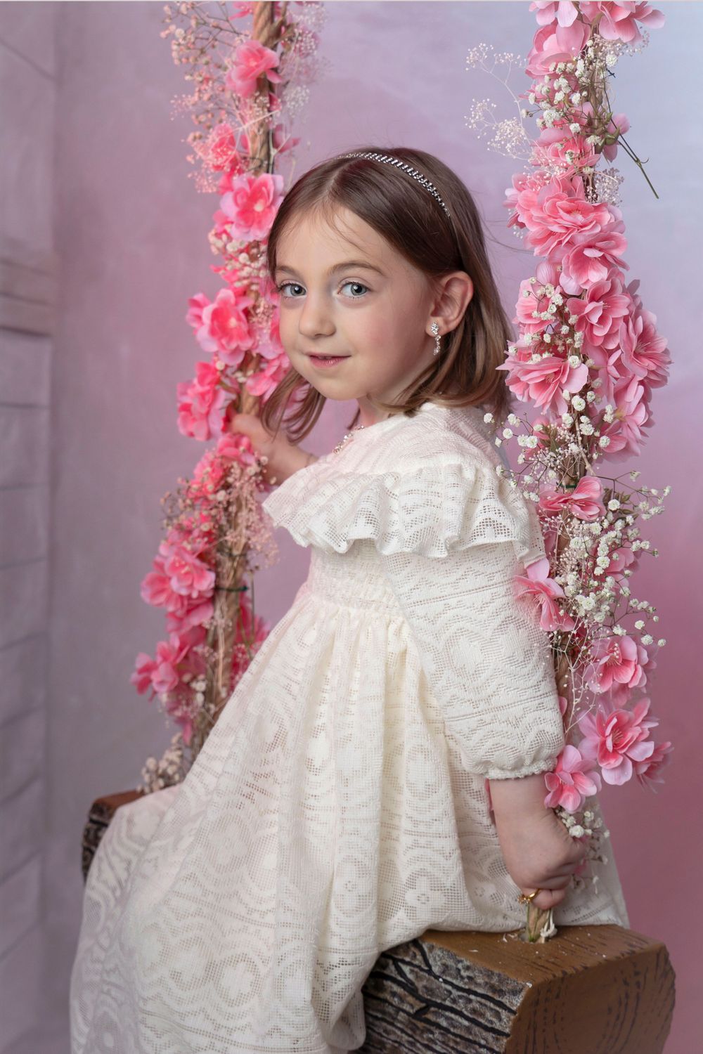 Vintage-inspired portrait with pink floral garland and white lace dress against pastel backdrop.