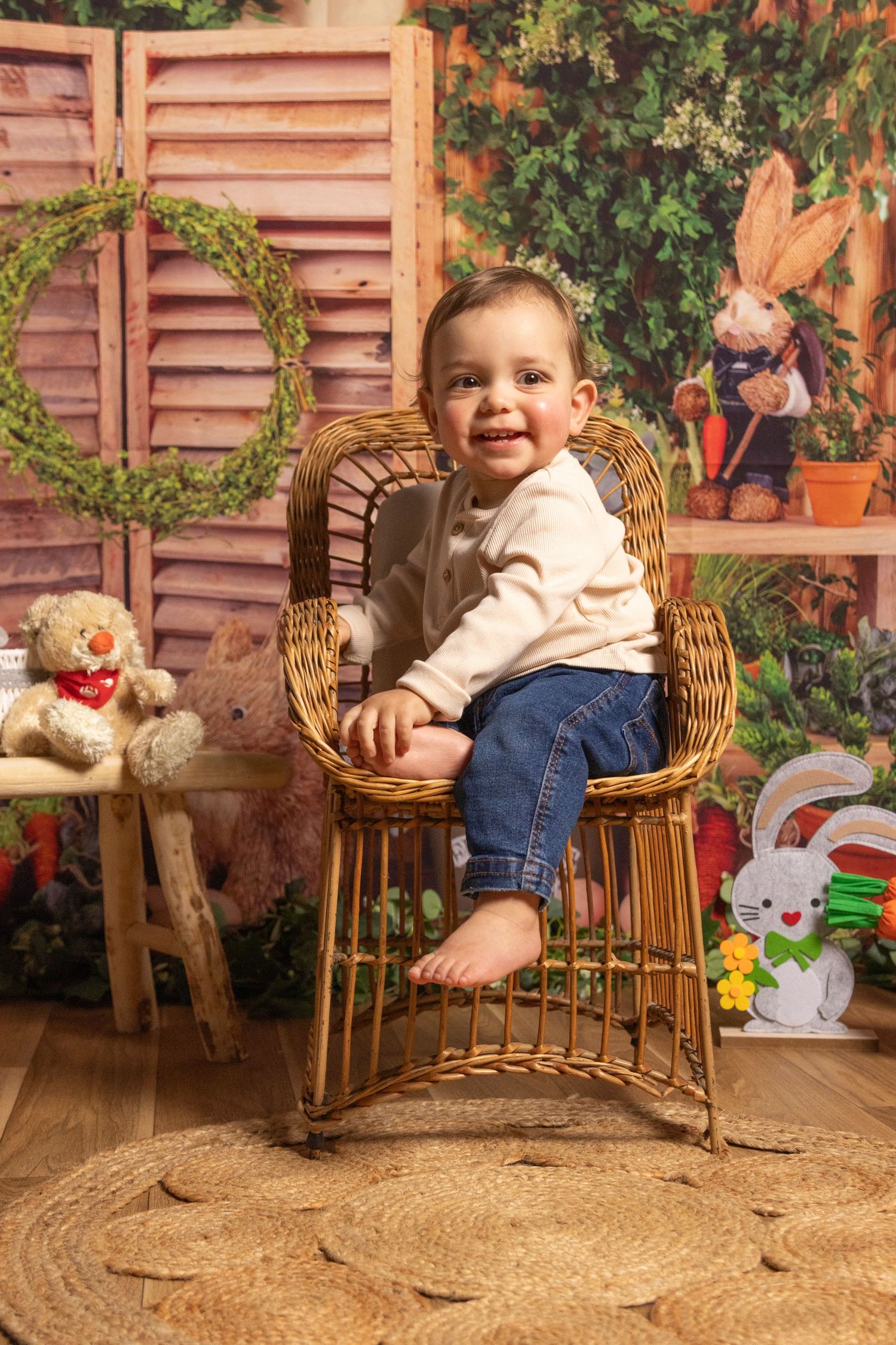 Happy toddler posing in wicker chair surrounded by fall decorations and plush toys.