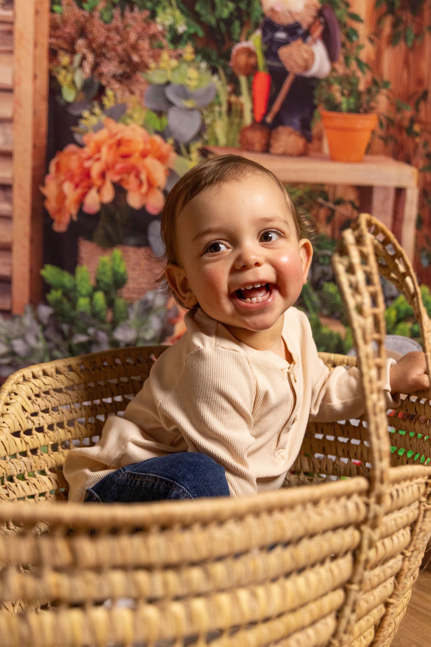 Smiling baby in cream sweater sitting in wicker basket with autumn decorative background.