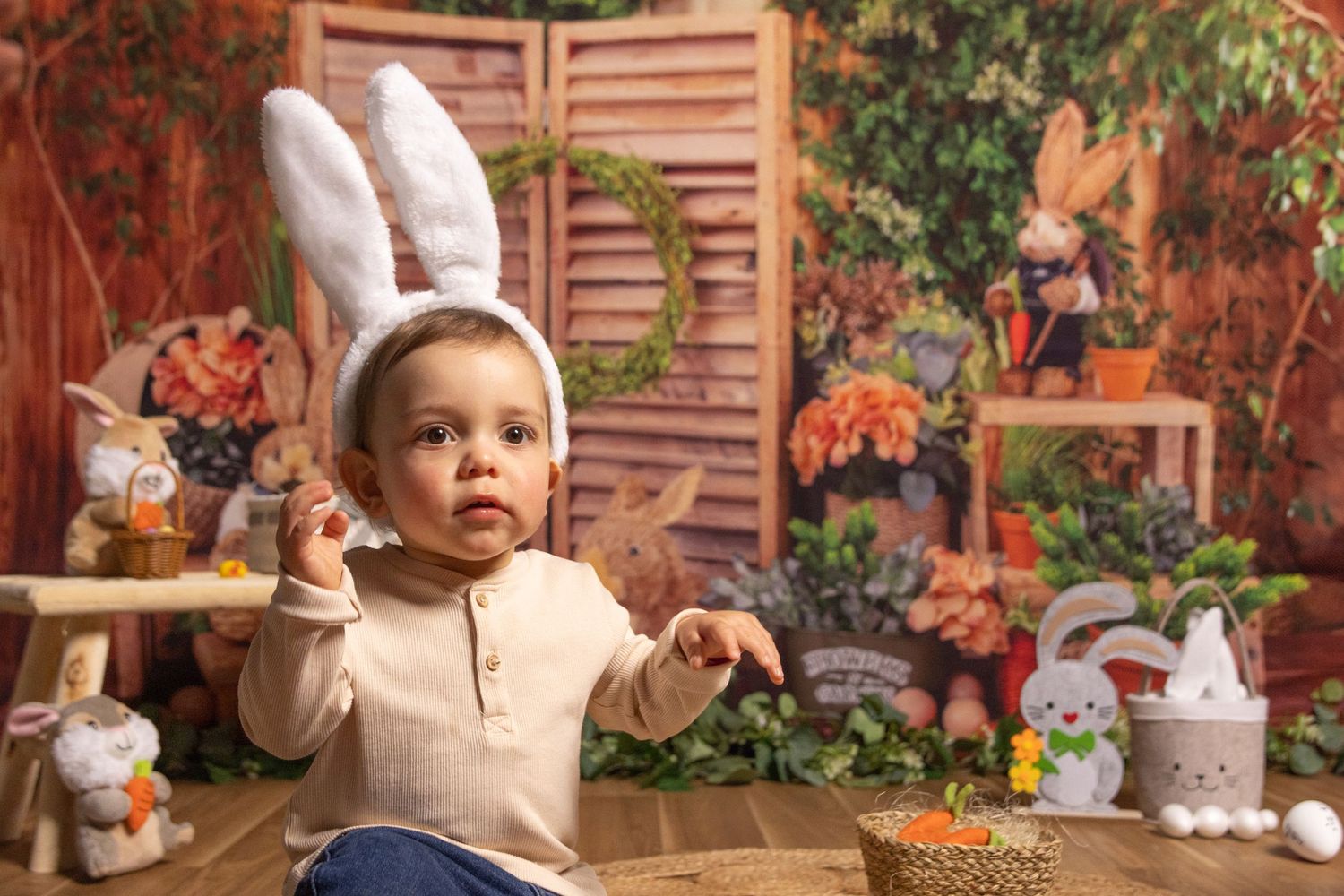 Baby in beige outfit laughing during fall-themed photo shoot with rustic wooden backdrop.