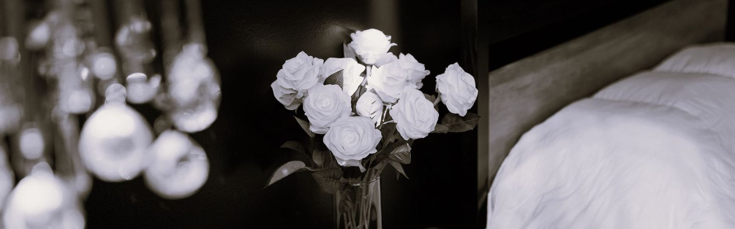Elegant white orchids in a glass vase against a black and white background with soft bedding visible.
