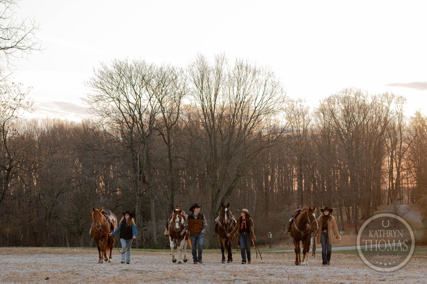 A group of riders on horseback gather at sunset with bare trees in the background.
