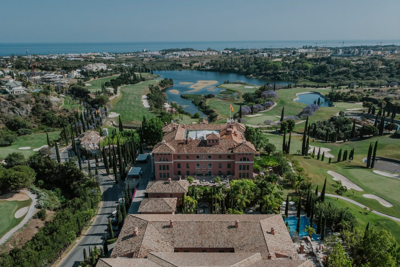 Aerial view of a luxury Mediterranean villa with terracotta roofs overlooking a golf course and coastline in Spain.