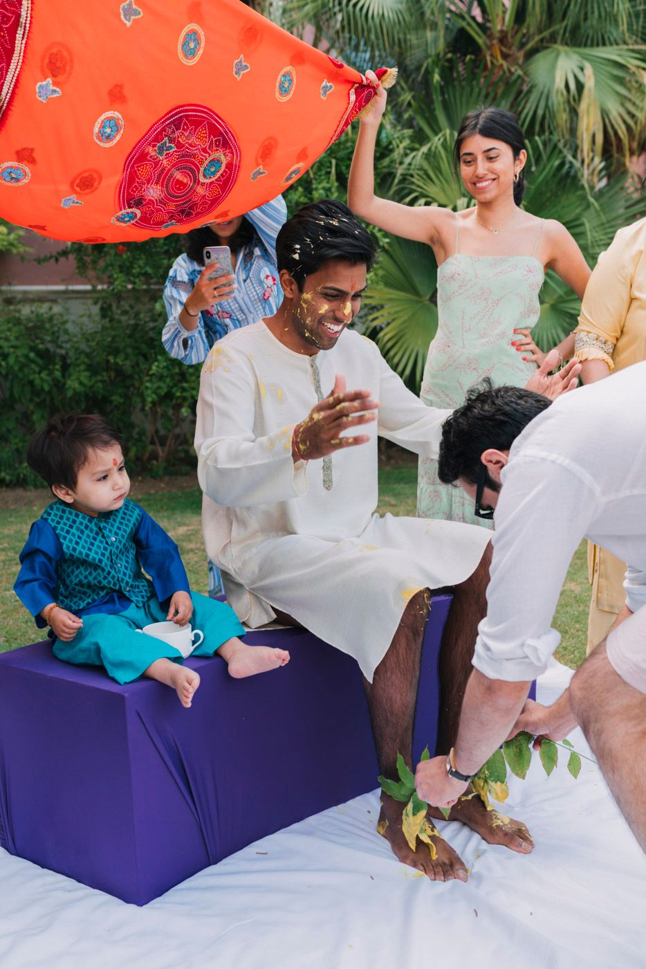 People enjoying a colorful outdoor gathering with someone sitting on a purple ottoman while others celebrate around them.