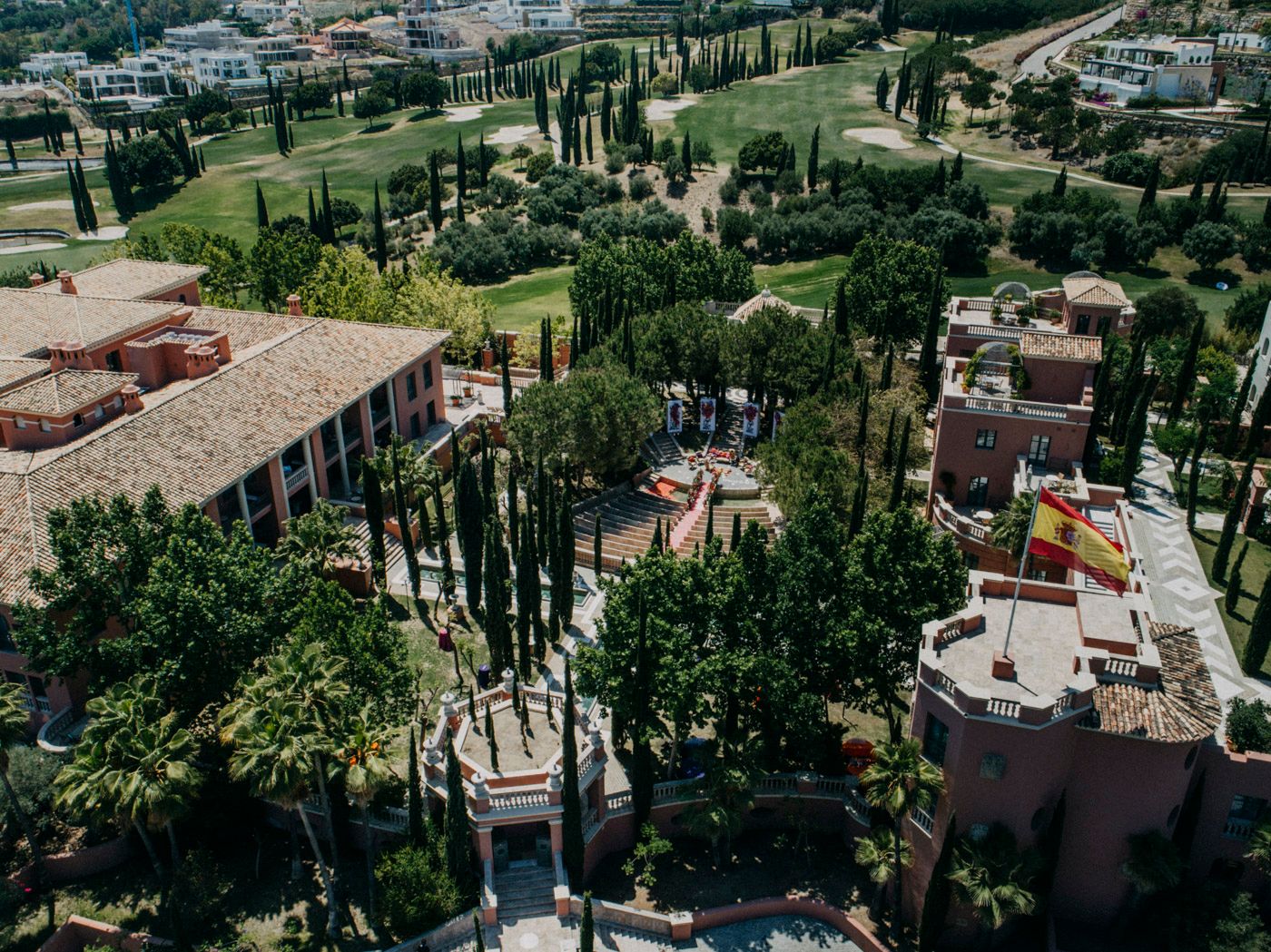 Aerial view of a Mediterranean villa complex with cypress trees, terracotta roofs, and manicured gardens.