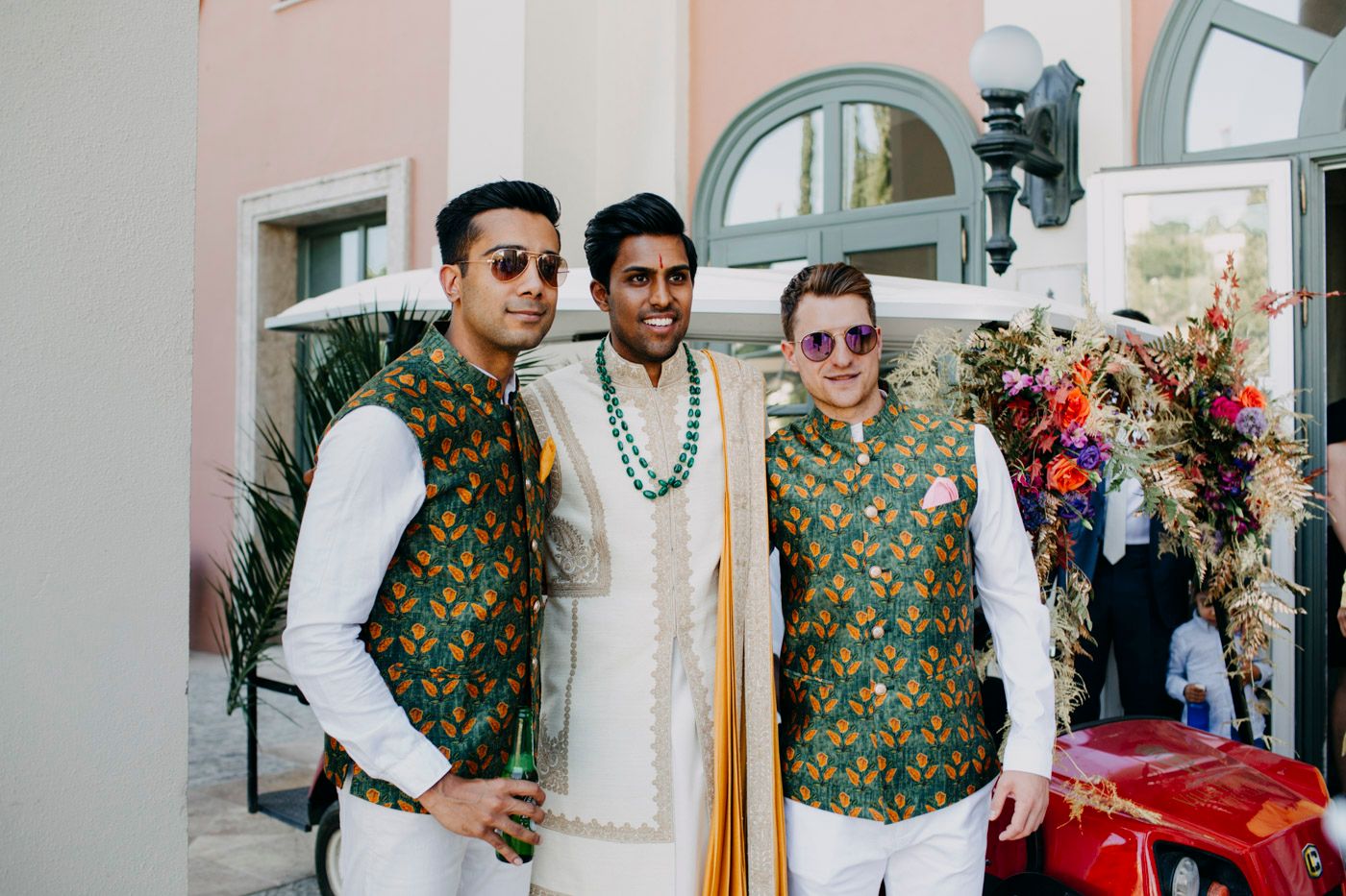 Three people wearing traditional Indian attire with matching green and gold brocade vests pose together at a formal event.