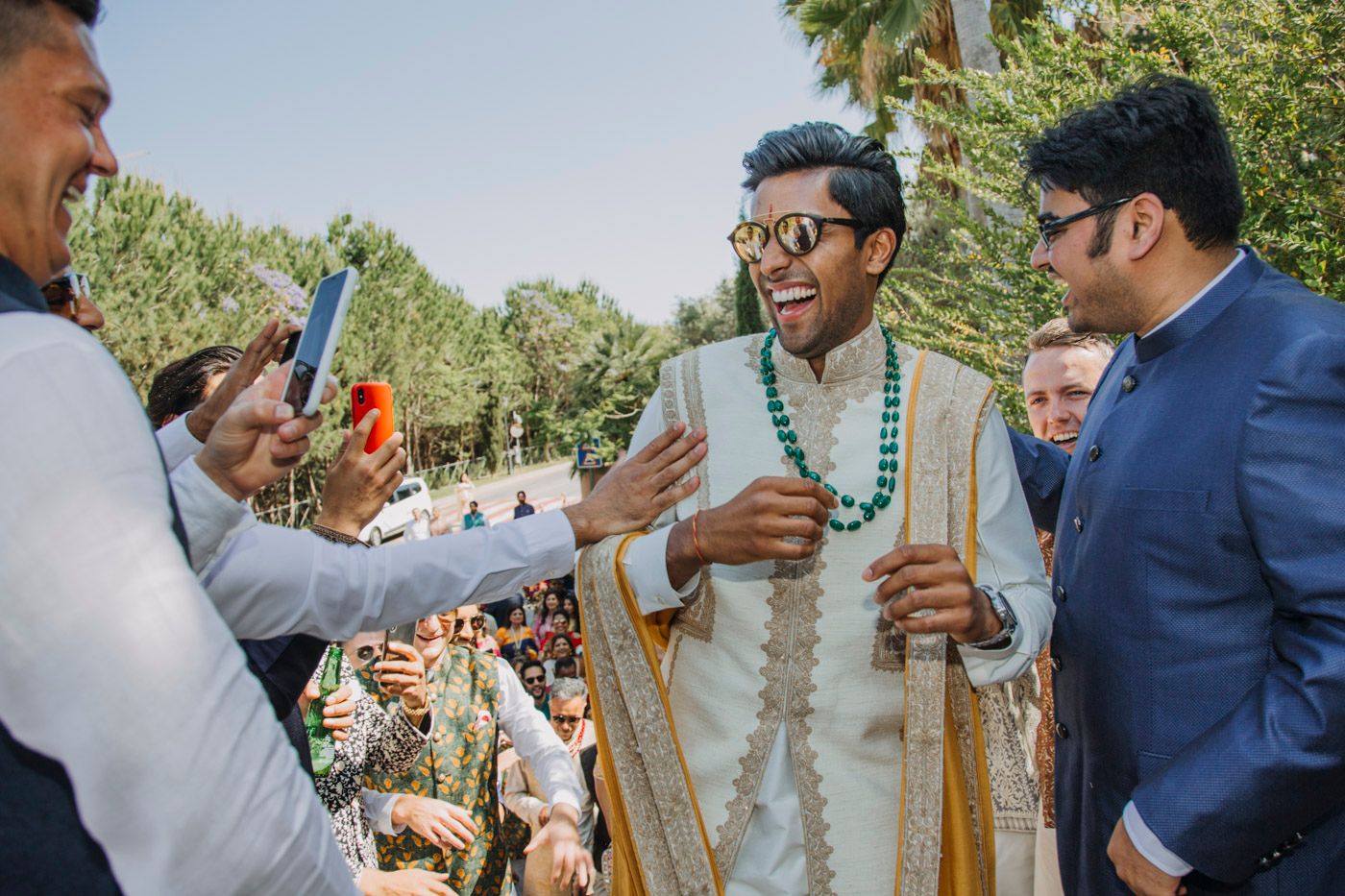 A festive traditional Indian wedding celebration outdoors with attendees in formal attire during a sunny day.