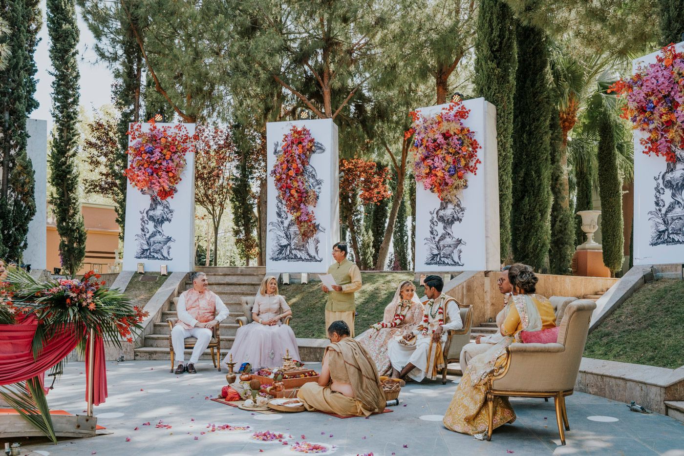 Elegant outdoor wedding reception setup with white floral pillars and vintage furniture arranged on a stone patio.