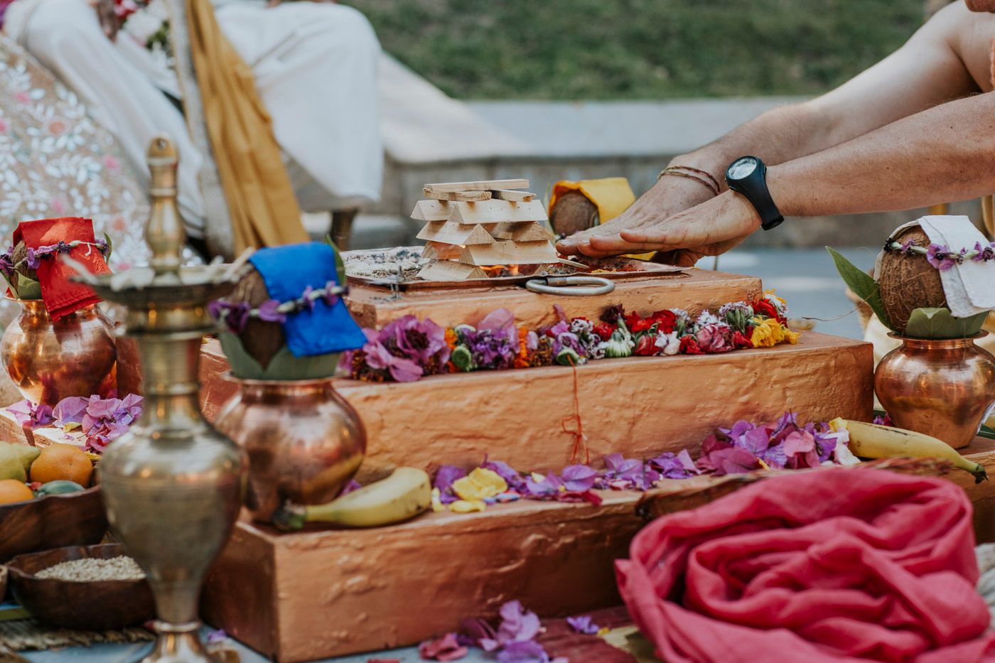 A wooden tray filled with colorful flowers and snacks on a picnic blanket with copper accents and drinks.
