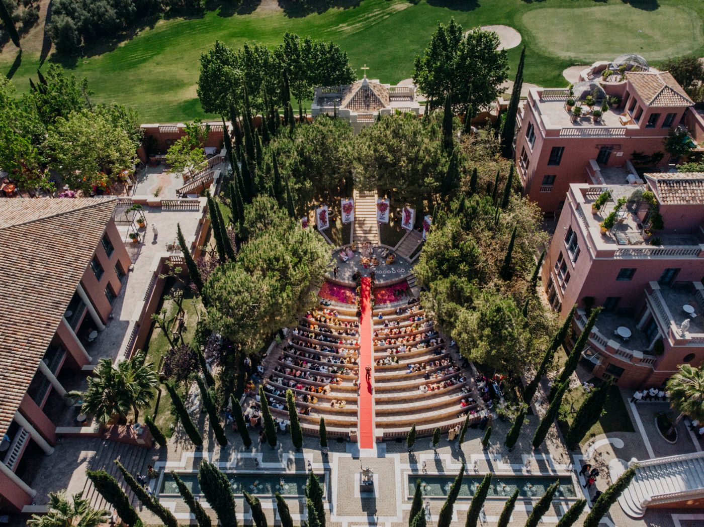 Aerial view of an outdoor wedding ceremony with rows of seats and decorative walkway surrounded by trees and buildings.
