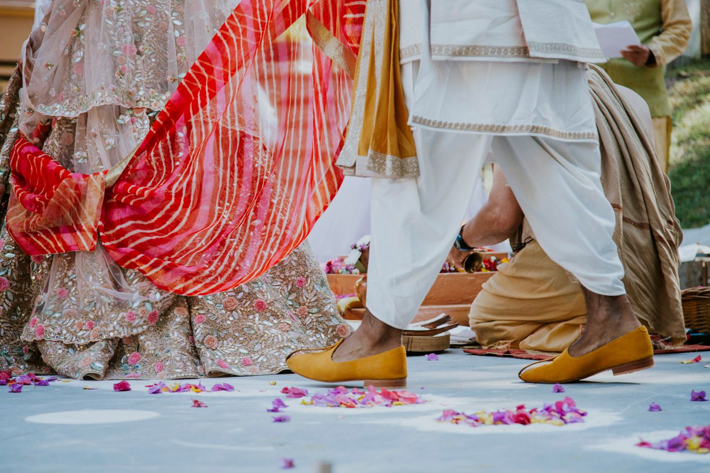 Close-up of traditional Indian wedding attire showing red and white garments with flower petals scattered on ground.