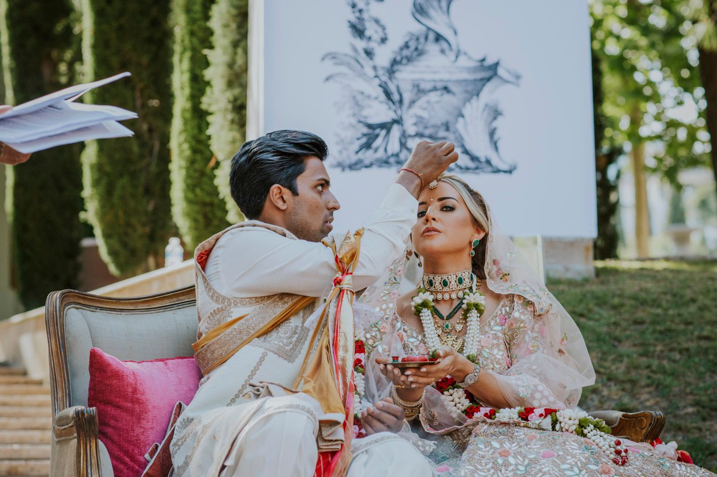 A traditional South Asian wedding ceremony taking place outdoors with bride and groom seated together in ceremonial attire.
