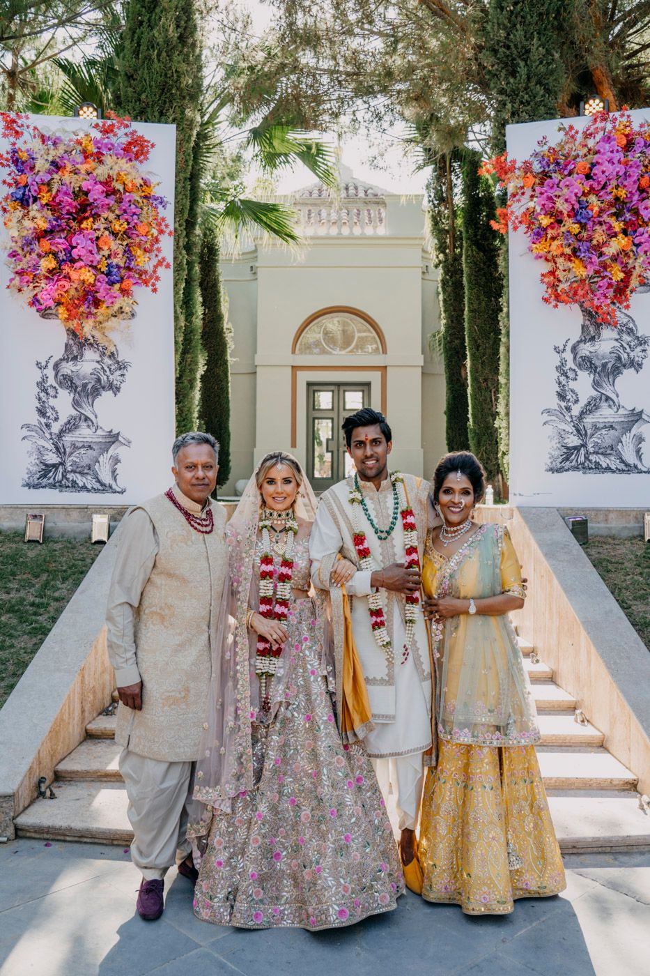 Elegant wedding ceremony scene on white marble steps with colorful floral arrangements framing a classical building entrance.