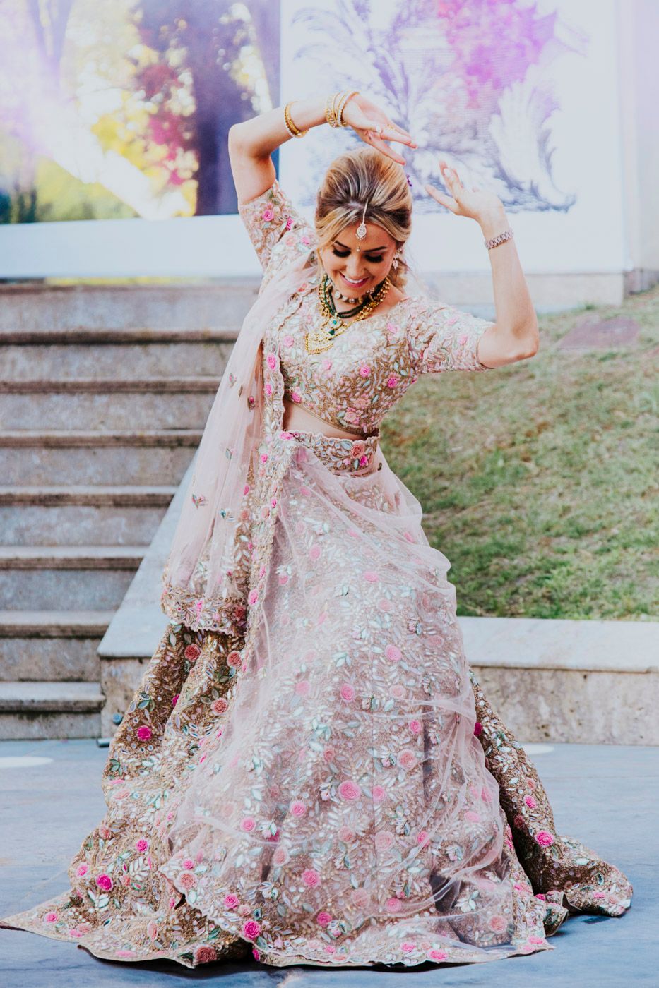 A beautiful pink and gold lehenga dress twirls gracefully on outdoor stone steps with a dreamy filtered effect.