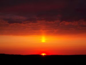 Dramatic orange sunset with glowing sun breaking through dark clouds on the horizon.