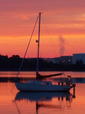 Sailboat silhouetted against vibrant orange sunset sky reflecting on calm harbor waters.
