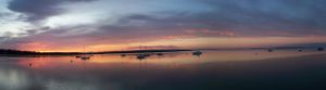 Panoramic view of boats silhouetted on calm water during a colorful sunset.