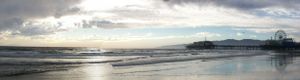Panoramic beach scene with dramatic clouds and sunlight reflecting off wet sand.