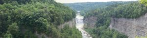 Panoramic view of a forested valley with waterfalls and rocky cliffs.