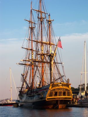 Historic tall ships with multiple masts docked at harbor during golden hour.
