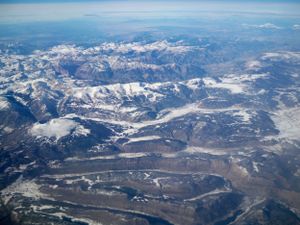Snow-covered mountain peaks and valleys seen from high altitude with scattered clouds below.