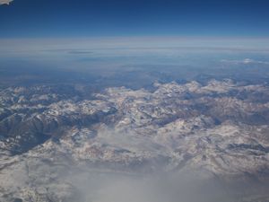 Aerial view of snow-capped mountain ranges extending to the horizon under bright blue skies.