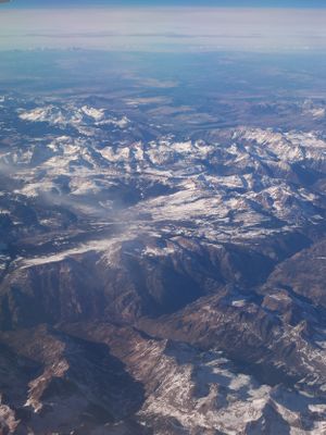 Bird's eye view of rugged mountain terrain with snow patches and deep valleys.