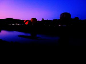 Silhouettes of hot air balloons against a vibrant purple and blue sunset sky.
