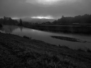 Moody black and white landscape of a winding river with mountains in the distance.