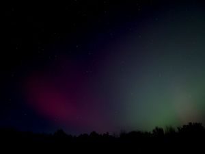 Purple and green aurora borealis shimmers above a dark landscape.