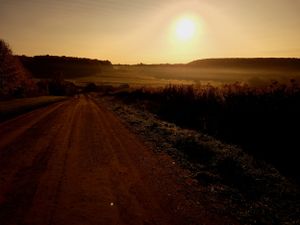 Dusty rural road stretches toward the horizon at sunset with golden sky.