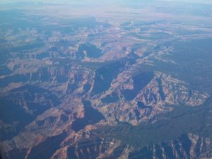 Sweeping aerial view of dramatic canyon formations and desert plateaus under blue skies.