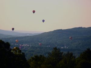 Multiple hot air balloons soar over a misty mountain valley during golden hour.