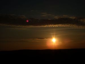 Dramatic sunset over dark silhouetted hills with golden sun peeking through clouds.