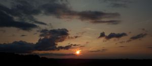 Dramatic clouds at sunset with sun rays piercing through dark sky.