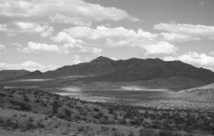 Desert mountain landscape under cloudy skies with rugged terrain stretching to the horizon.
