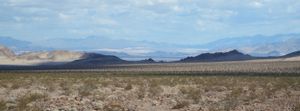 Panoramic view of arid desert valley with distant mountain ranges and blue sky.