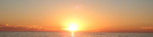 Dramatic orange sunset over calm water with vibrant sky colors.