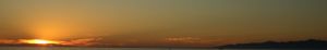 Golden sunset silhouette over dark horizon with warm glowing sky.